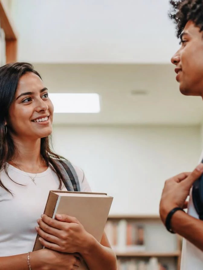 Duas participantes conversando de pé no corredor entre prateleiras de livros